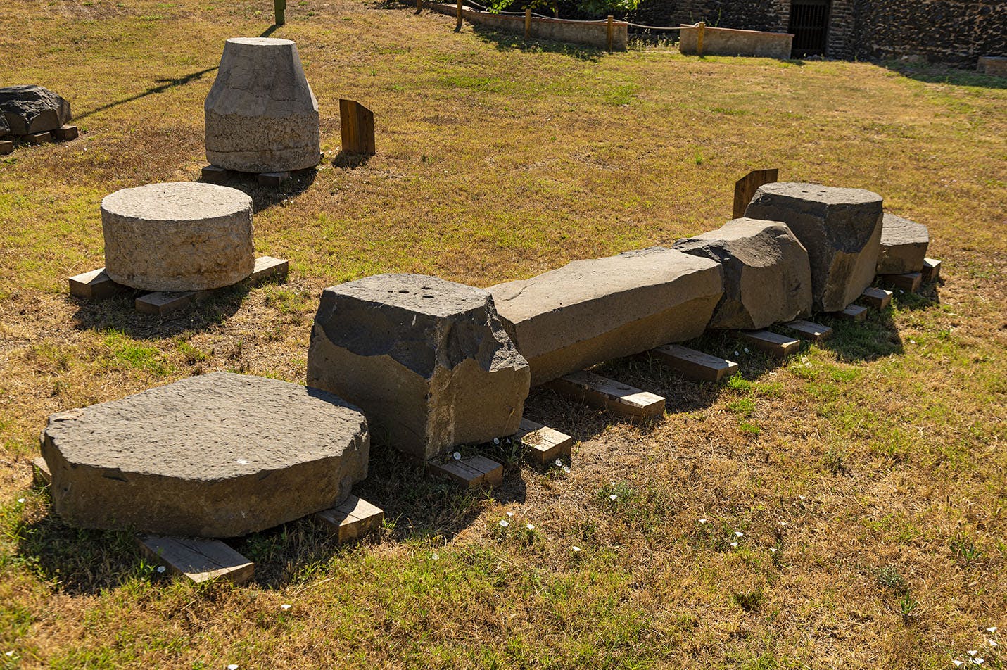 Stone ruins including columns and cylindrical blocks scattered on a grassy area.