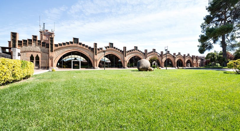 Un bâtiment aux grandes fenêtres cintrées et à la maçonnerie en briques, sur fond d'herbe et de ciel bleu clair.