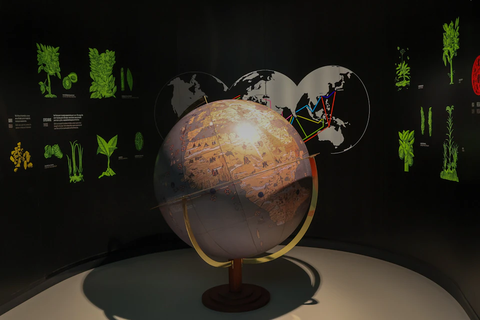 A globe displayed in a dimly lit room with illuminated maps and diagrams on the surrounding walls.