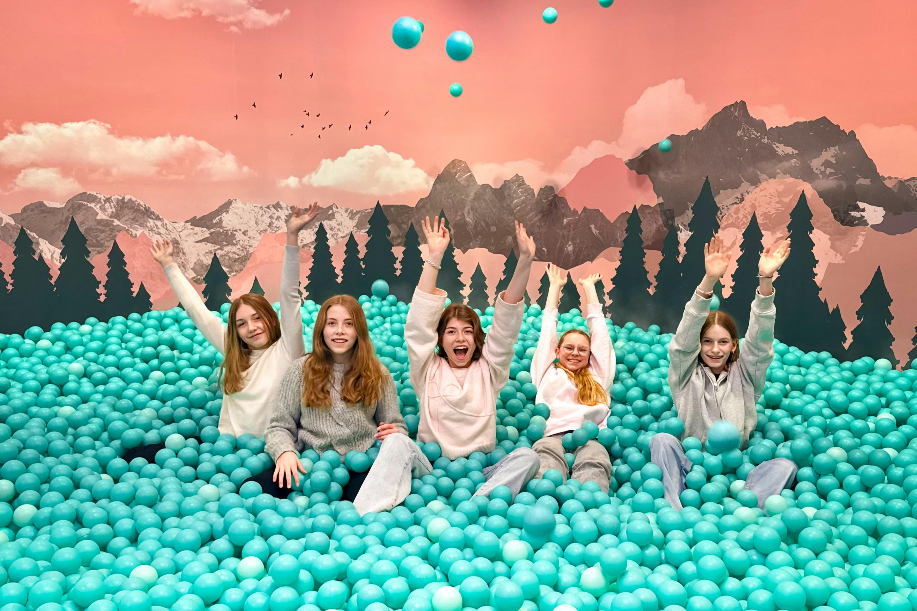 マジックバイエルンの遊び心溢れるフォトスポット、高山を背景にした巨大なターコイズ色のボールピットで楽しむ5人の女の子たち