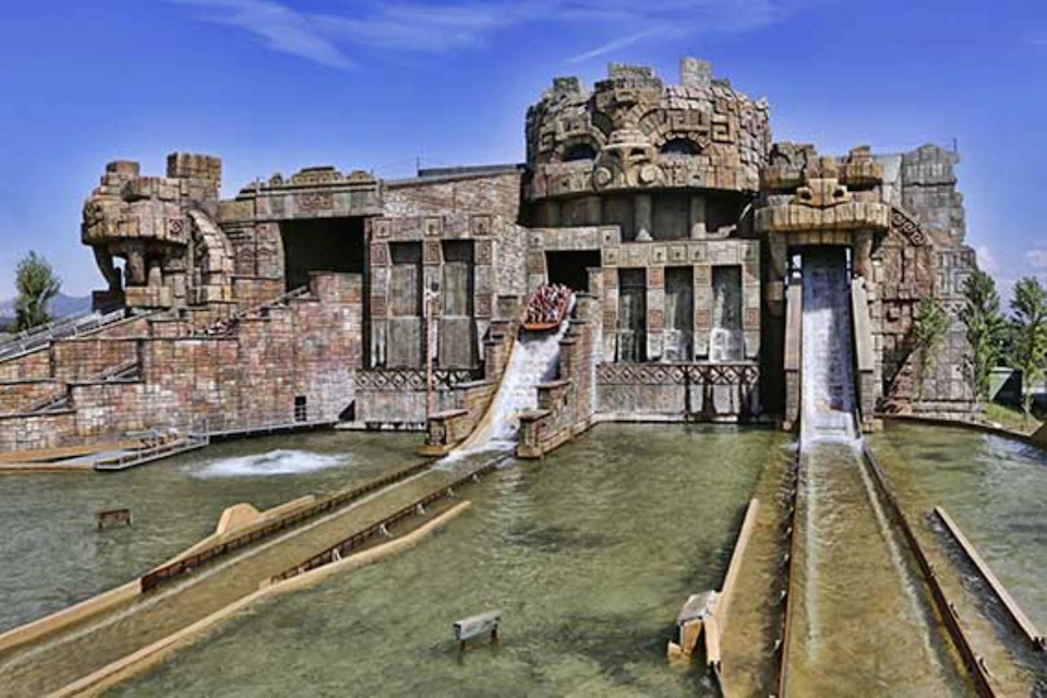 Stone-themed water ride with slides and a boat descending with passengers, surrounded by carvings and structures resembling ruins.