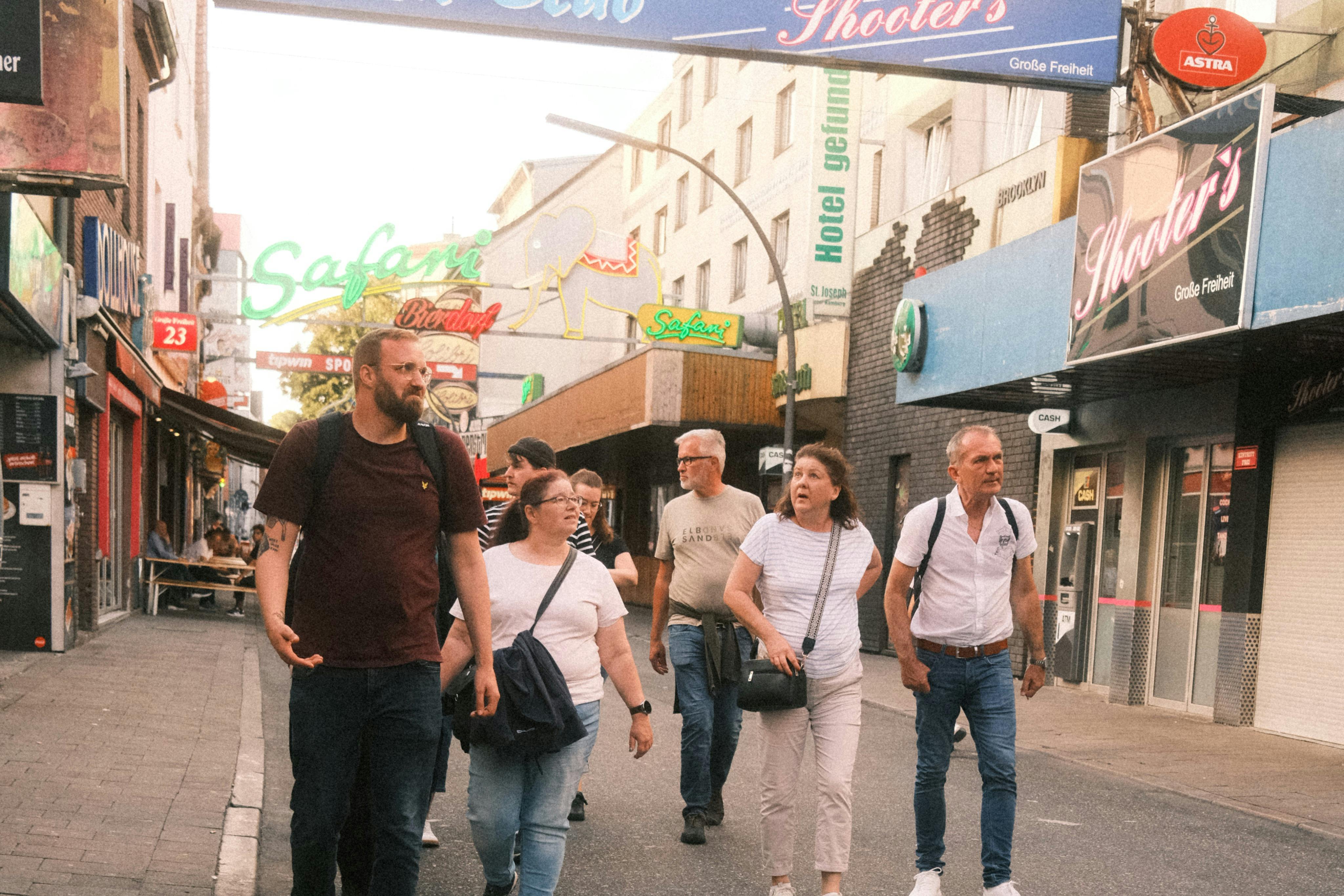 Μια ομάδα ανθρώπων περπατά σε έναν δρόμο γεμάτο καταστήματα και πινακίδες νέον σε μια αστική περιοχή.