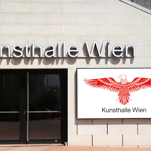 Entré till Kunsthalle Wien med stora glasdörrar och en röd örn-logotyp med texten "Kunsthalle Wien" på en skylt.