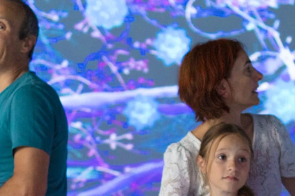 A group of five people standing in an immersive room with colorful, abstract, and vibrant digital projections on the walls.