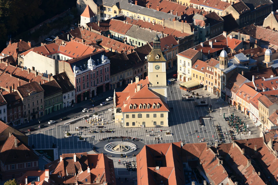 Aerial view of a historic town square with a clock tower, surrounded by colorful buildings with red roofs.