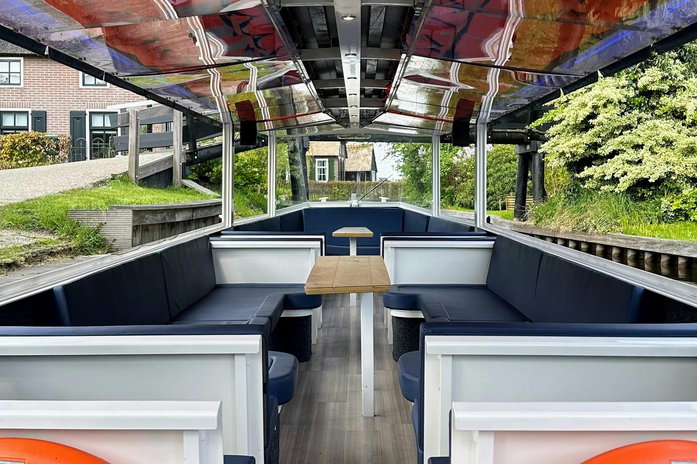 Intérieur d'un bateau de canal vide avec des bancs rembourrés, des tables en bois et de grandes fenêtres montrant un paysage extérieur verdoyant.