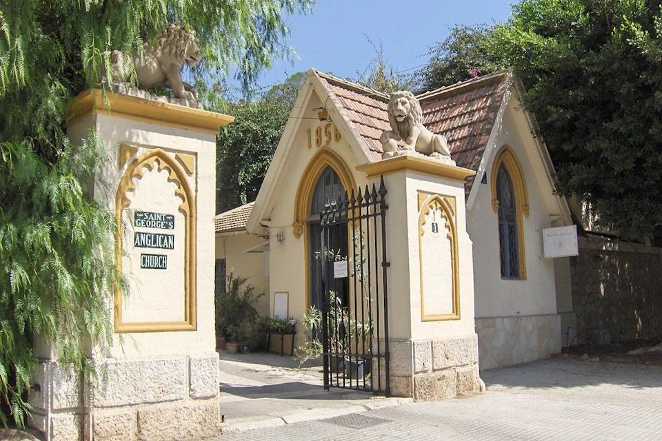 Ornate entrance gate to Saint George's Anglican Church with lion statues, arched door, and lush greenery.