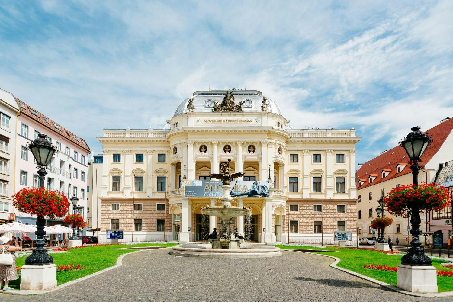装饰华丽的剧院，大横幅、中央圆顶和前面的喷泉，周围环绕着维护良好的绿色草坪。