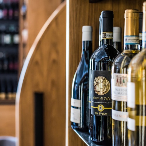 Bottles of wine are displayed on shelves in a wine shop with a wooden backdrop.