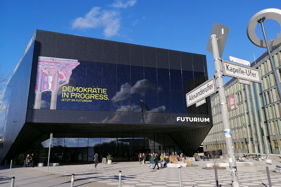 Modern black building with reflective glass facade, a sign reading 'Futurium,' and people near the entrance.