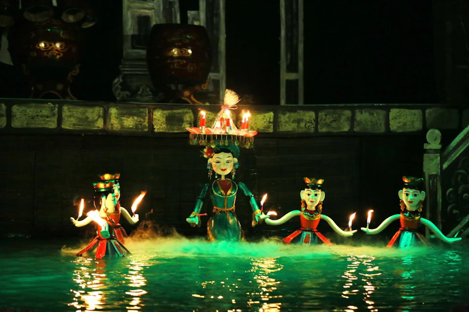 Water puppets performing on a pool, featuring colorful figures holding candles, against a lit-up dark background.