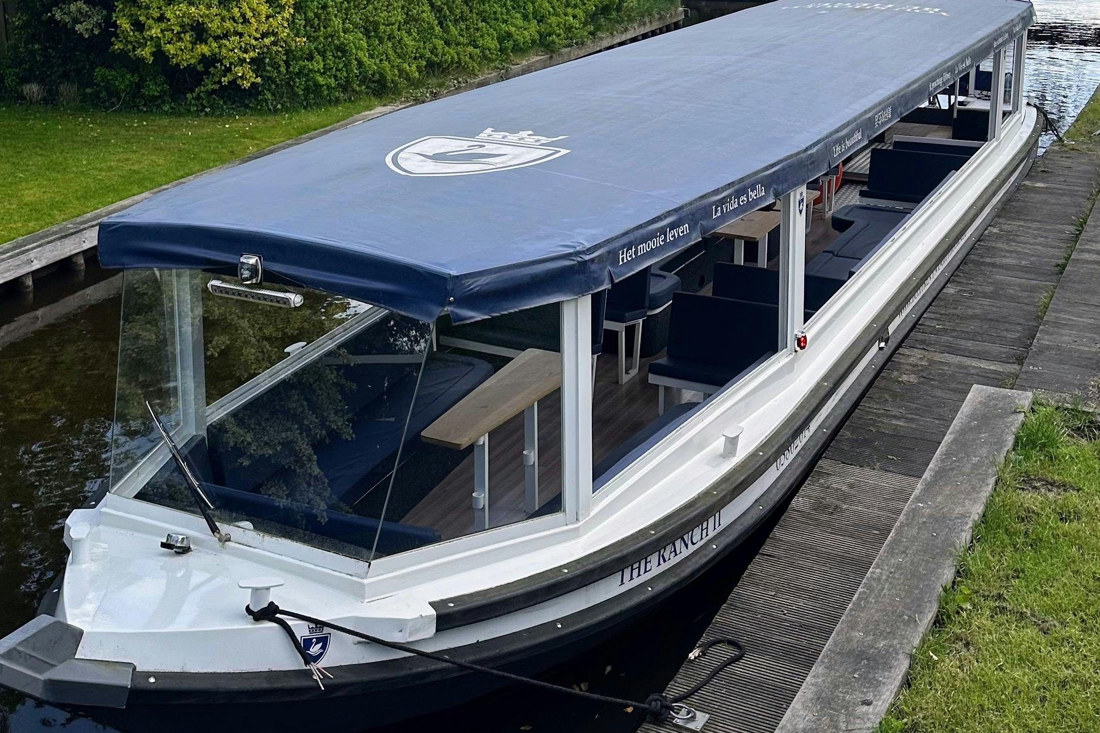 Bateau touristique couvert, amarré au bord d'un canal, doté de vitres et de sièges pour les passagers.
