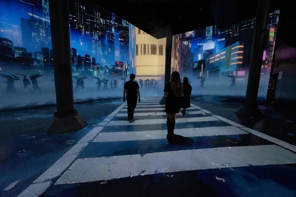 People walk on a zebra crossing in a futuristic, foggy cityscape with illuminated buildings and digital projections.