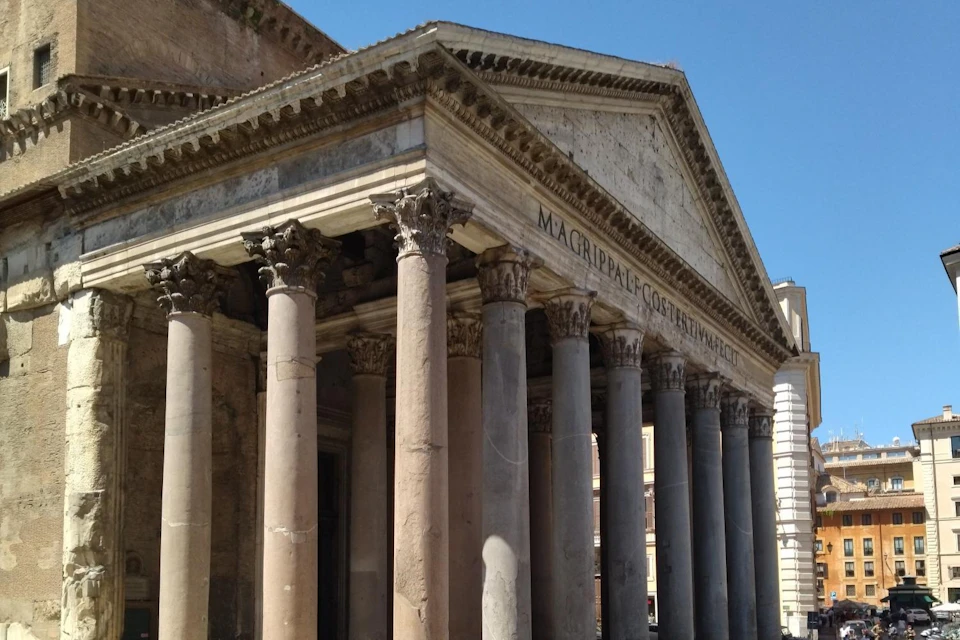 Ancient Roman temple with grand columns and a pediment featuring Latin inscriptions, set against a clear blue sky.