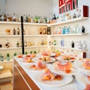 A bar setup with shelves full of various bottles and plates of appetizers with sliced meat and melon on a counter.