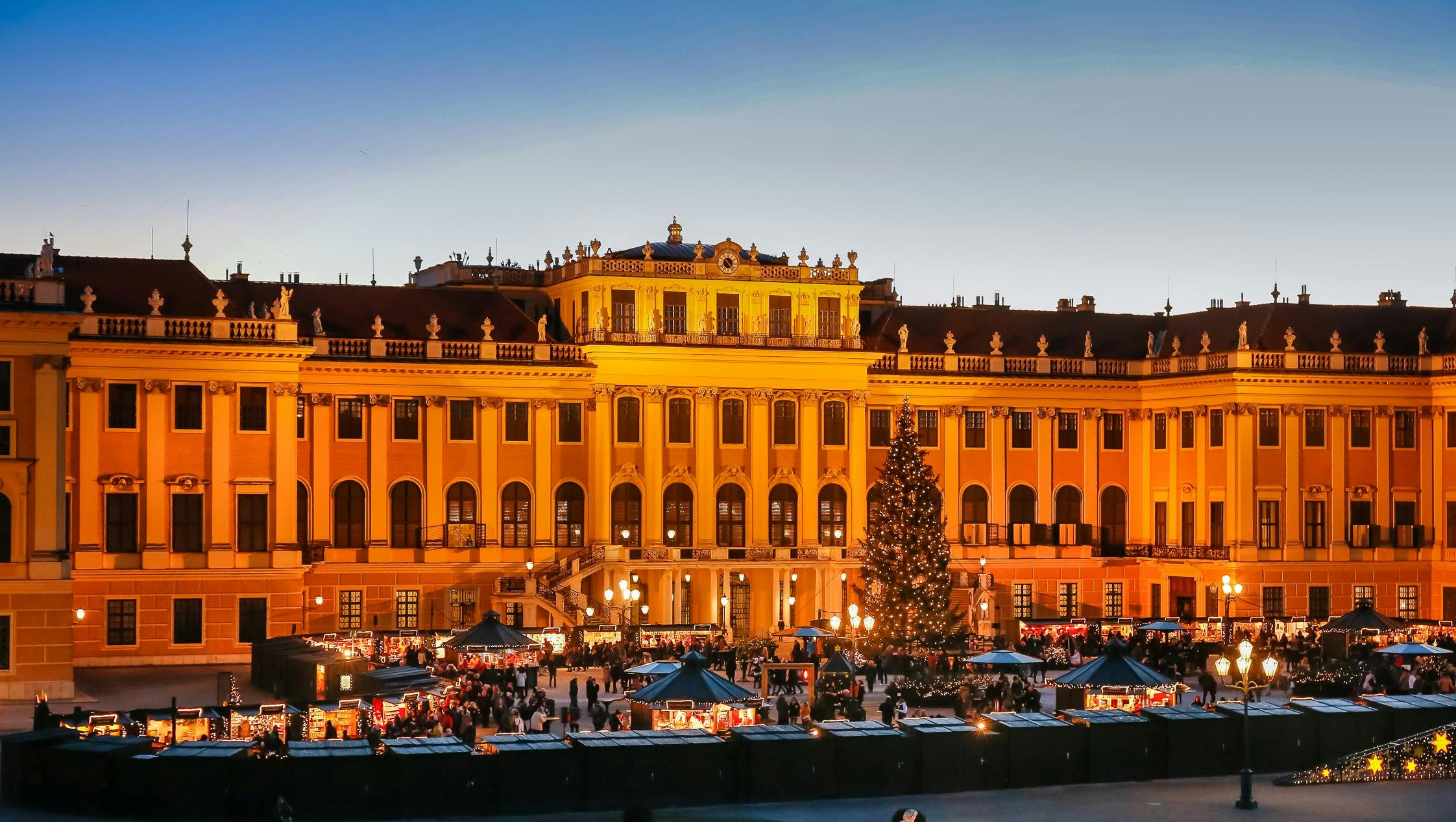 해질 무렵에 크리스마스 트리 장식과 번화한 야외 시장이 있는 커다란 조명 건물입니다.