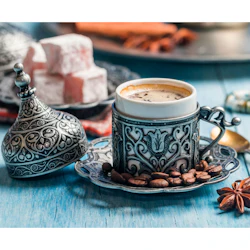 Ett turkiskt kaffeset med en kopp i utsmyckad hållare, omgiven av kaffebönor, stjärnanis och turkisk glädje på en blå träyta.