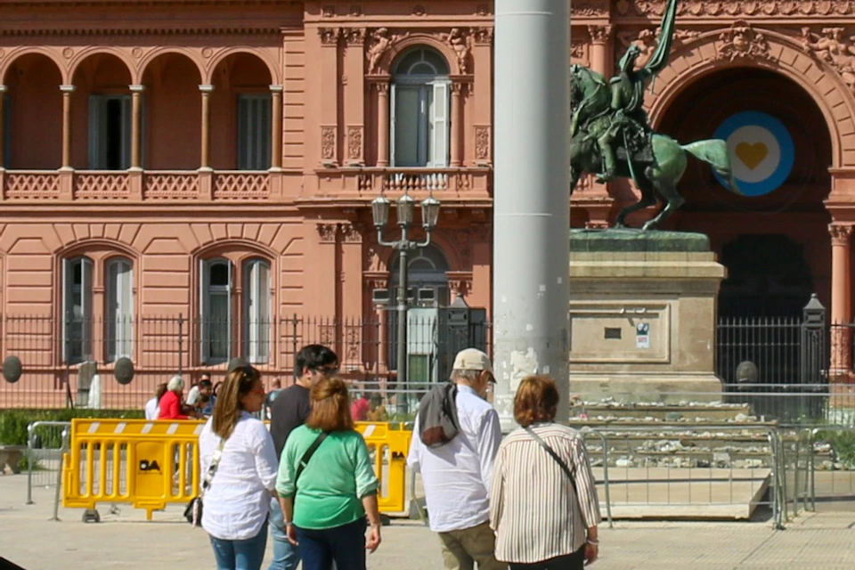 A guide speaking to a group in front of a pink historic building under a clear blue sky.