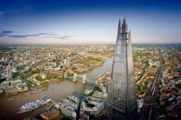 Statua della Regina Vittoria di fronte a Kensington Palace, circondata da un laghetto circolare e da prati curati sotto un cielo azzurro.