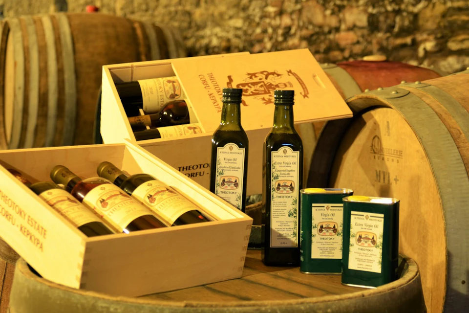Wooden crates with wine bottles, two olive oil bottles, and two olive oil tins on a wooden barrel with a rustic background.