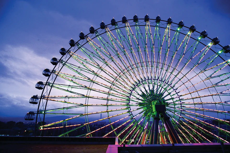 A large illuminated Ferris wheel with vibrant lights, set against a twilight sky.
