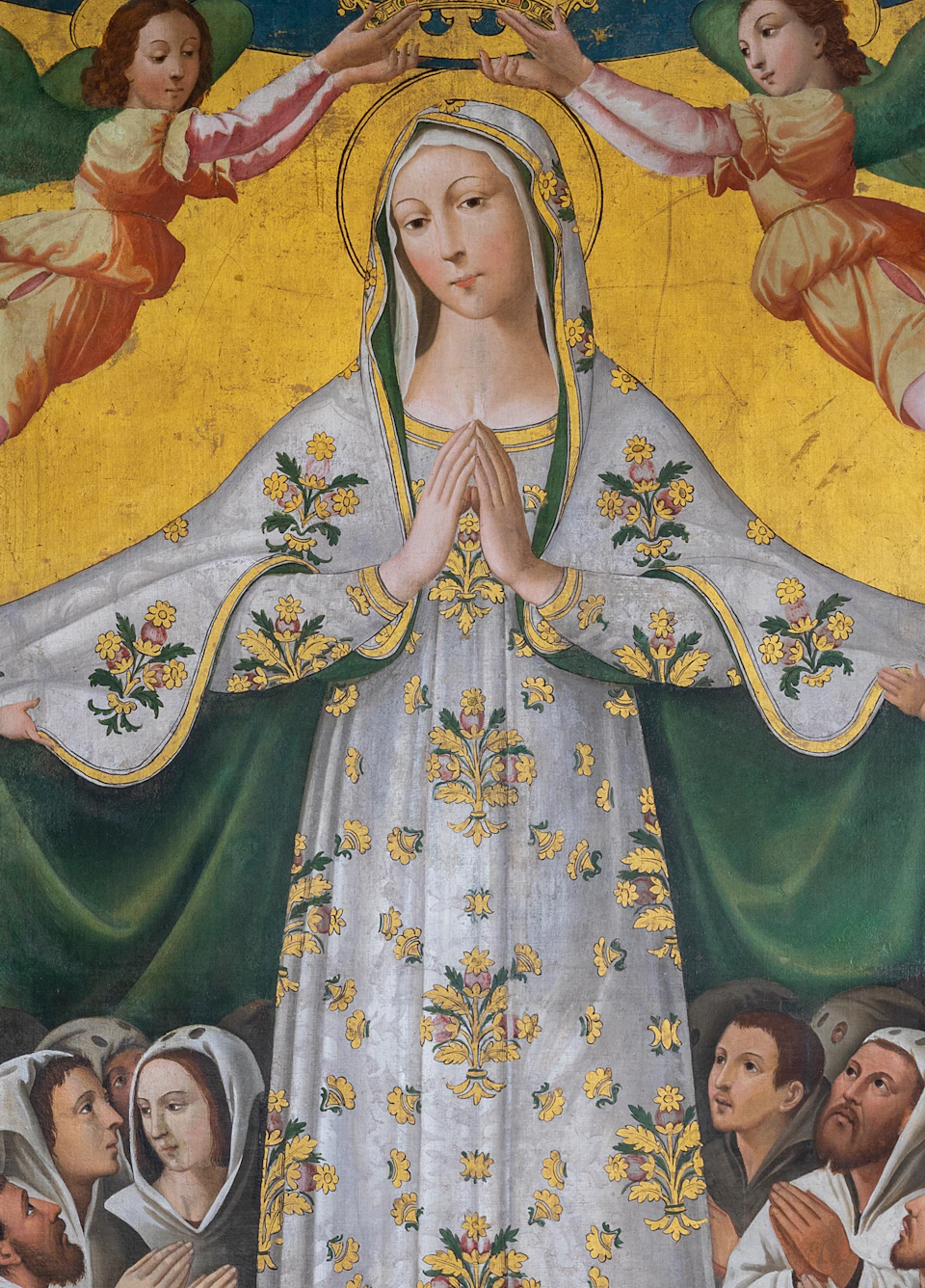 A painting depicts the Virgin Mary in a white robe with gold details, being crowned by two angels, surrounded by praying figures.