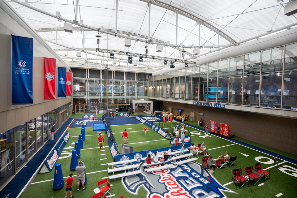 Indoor sports field with banners, goalposts, benches, and people engaging in activities under a glass ceiling.