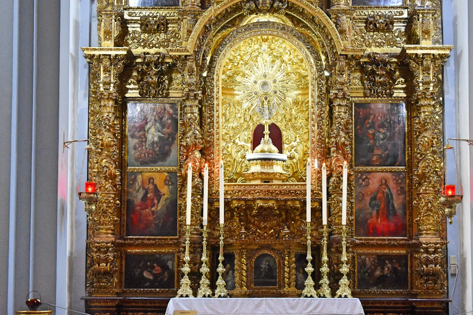 An ornate, golden altarpiece adorned with religious paintings, six tall candlesticks, and an intricately detailed sunburst.