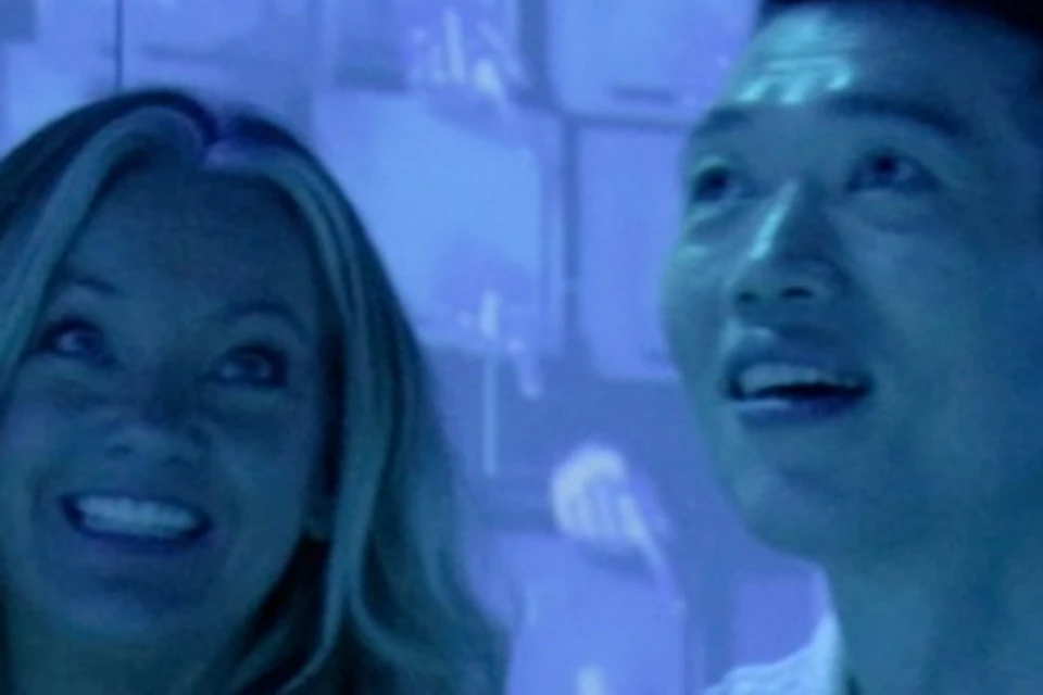 A family of four sits on a checkered floor, smiling and surrounded by blue-lit, abstract digital projections on the walls.