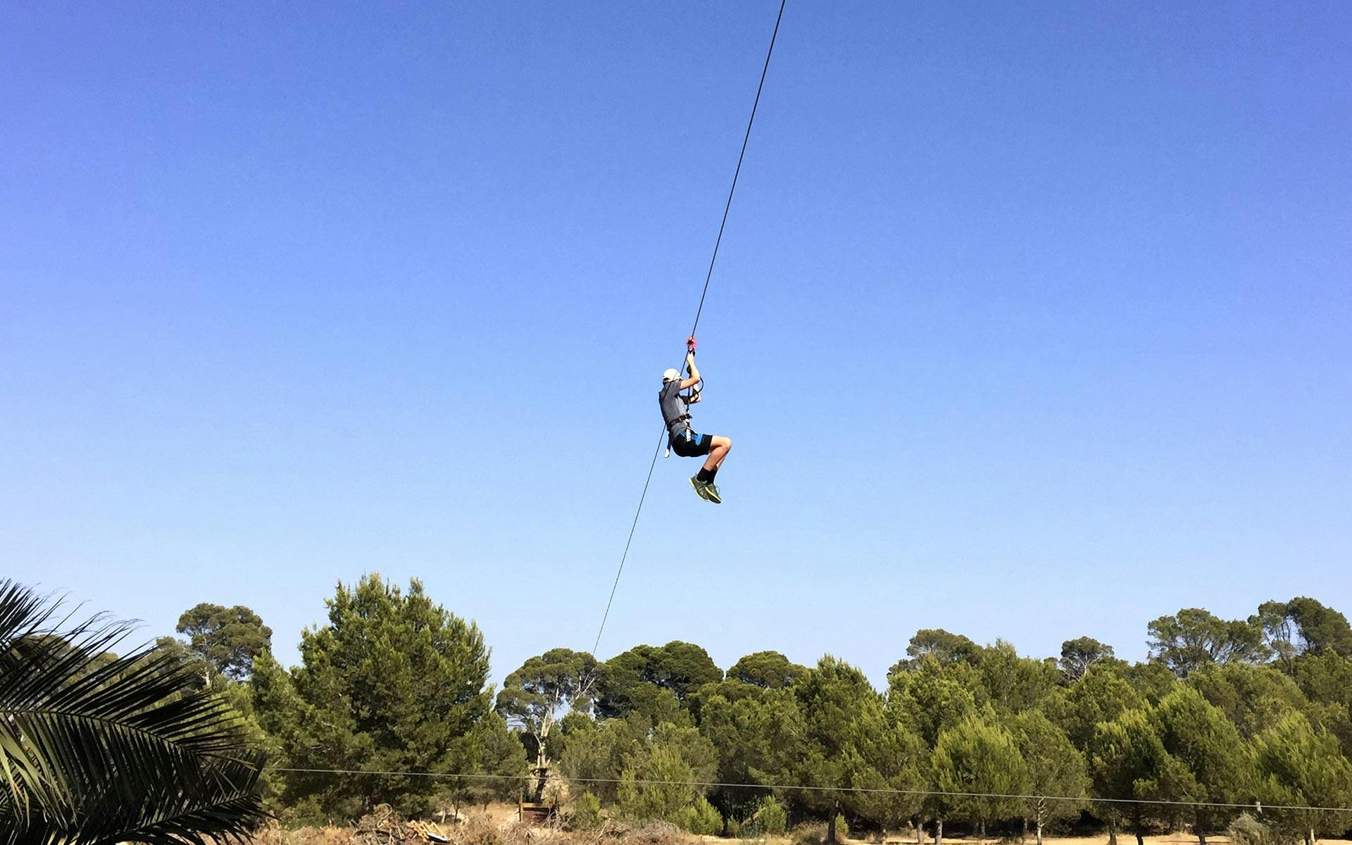 Person zip lining over a forested area under a clear blue sky.