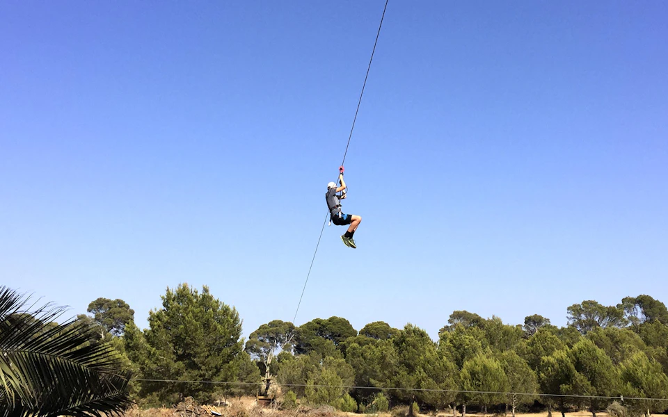 Person zip lining over a forested area under a clear blue sky.