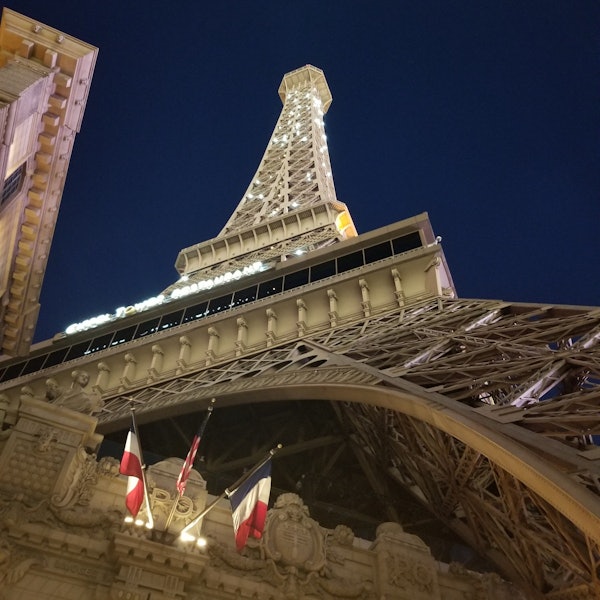 De replica van de Eiffeltoren bij nacht, verlicht en met Franse vlaggen aan de voet.