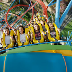 Människor på en ljusgul berg- och dalbana, skrikande och leende, medan åkturen dyker med öglor och spår synliga i bakgrunden.