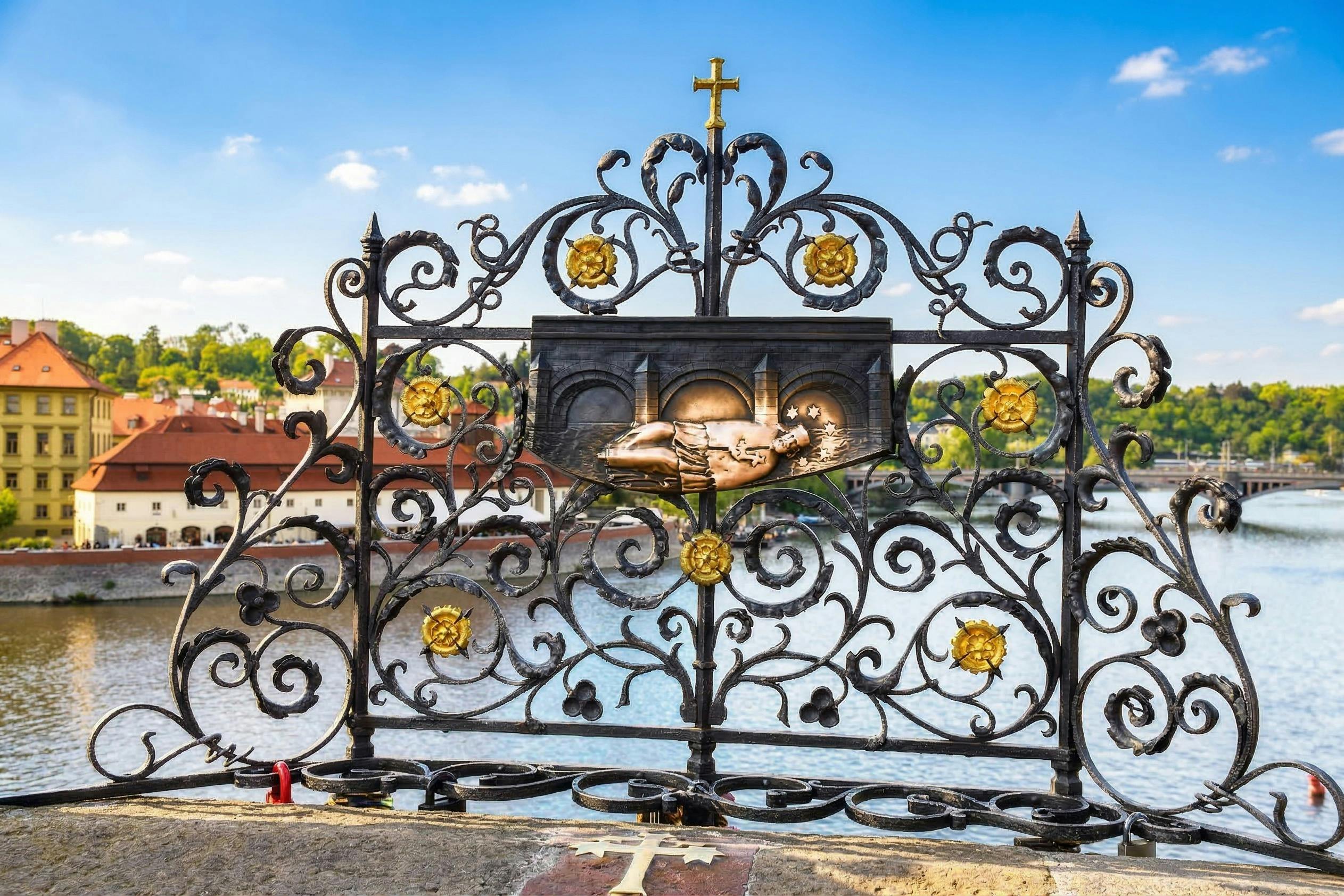 Ornate black iron gate with gold accents and a relief of a figure, set against a river and cityscape under a blue sky.