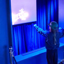En person i en grön hatt interagerar med en digital utställning och gör gester framför en skärm som visar ljus grafik.