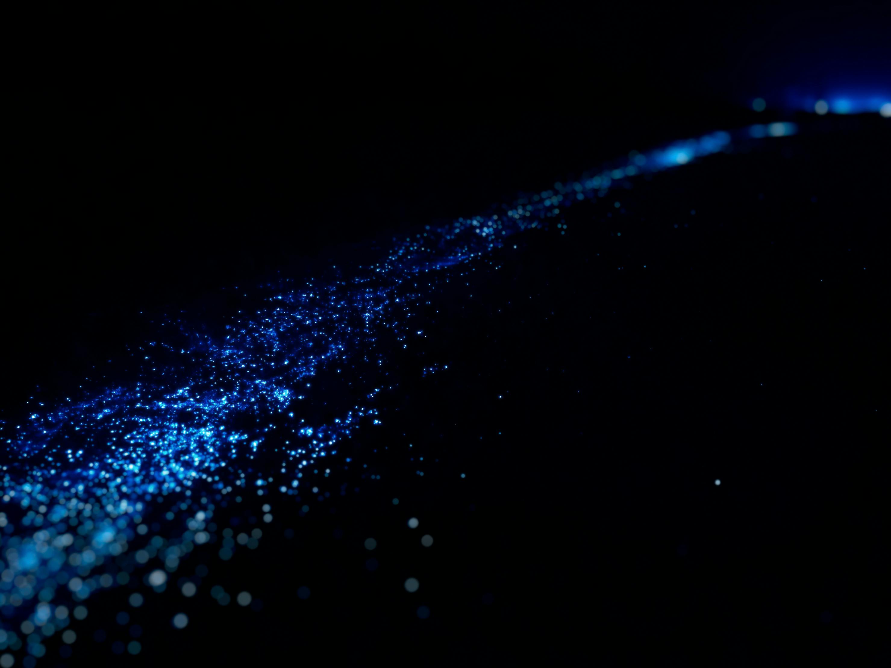 Des points de lumière bleus dispersés sur un fond noir et sombre, ressemblant à un ciel étoilé.