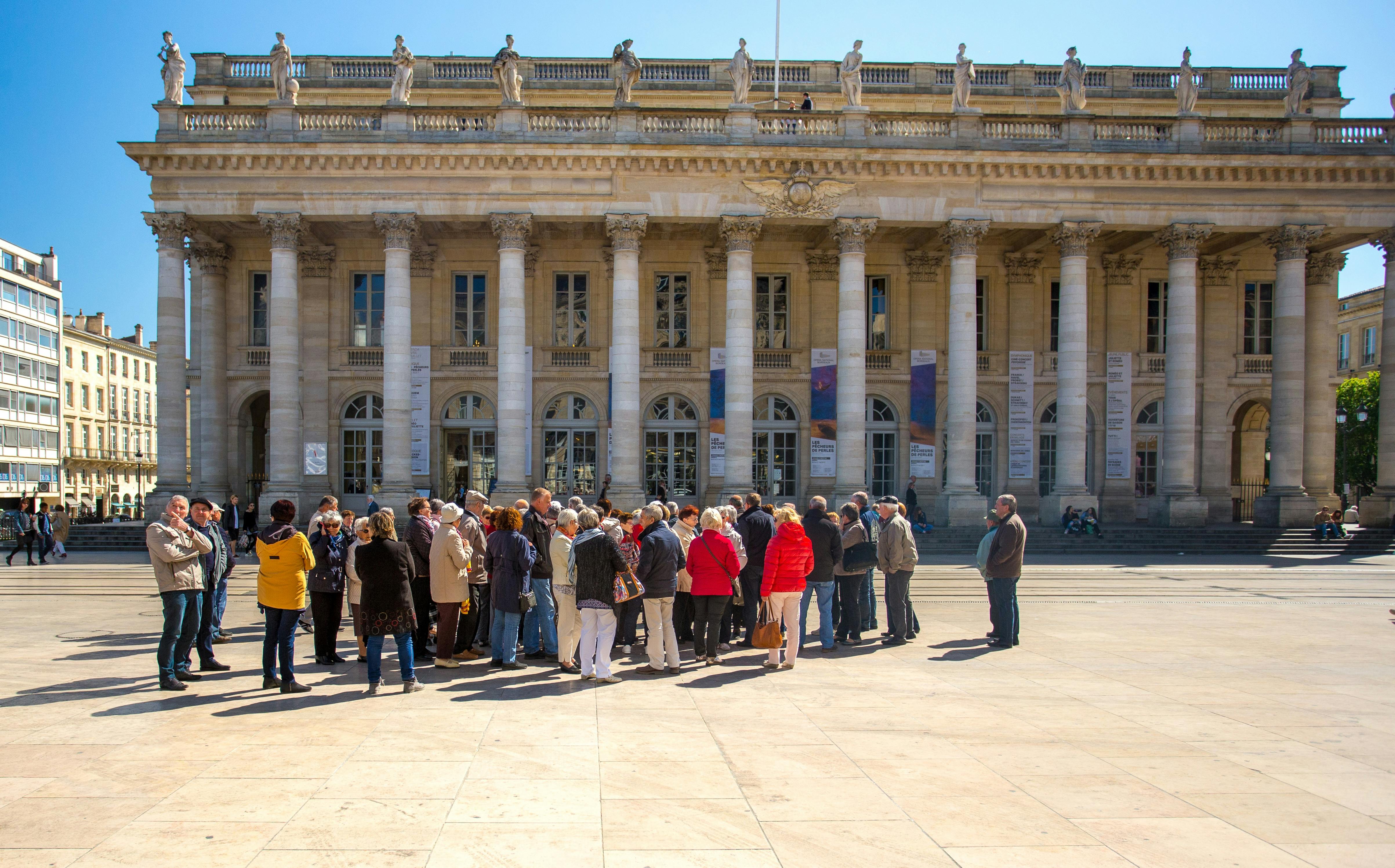 A group of people gather in front of a large neoclassical building with tall columns and statues on the roof.