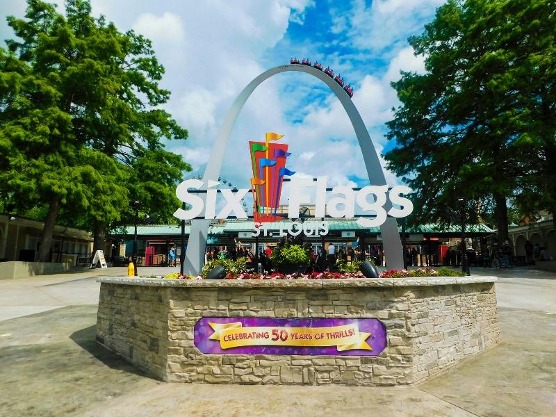 Wstęp na Six Flags St. Louis z ozdobnym łukiem i kolorowymi flagami. Na poniższym banerze jest napisane „Celebrating 50 Years of Thrills!”