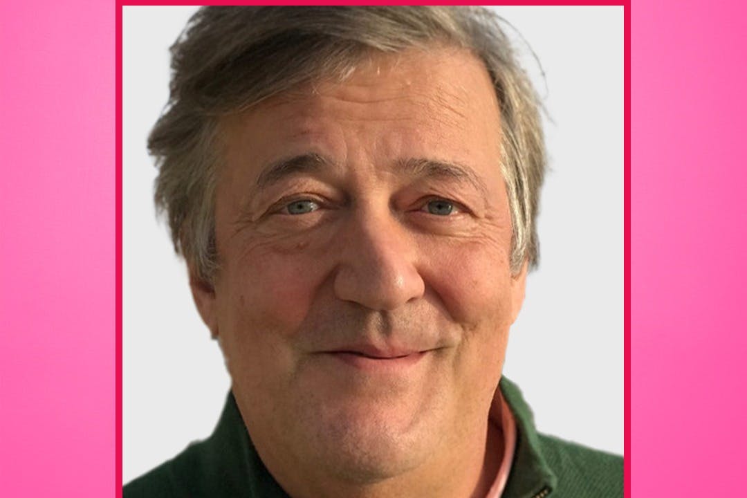 Ένας άντρας με γκρίζα μαλλιά και ένα ελαφρύ χαμόγελο, που φοράει ένα πράσινο πουλόβερ, φαίνεται σε ένα απλό φόντο με ροζ περίγραμμα.