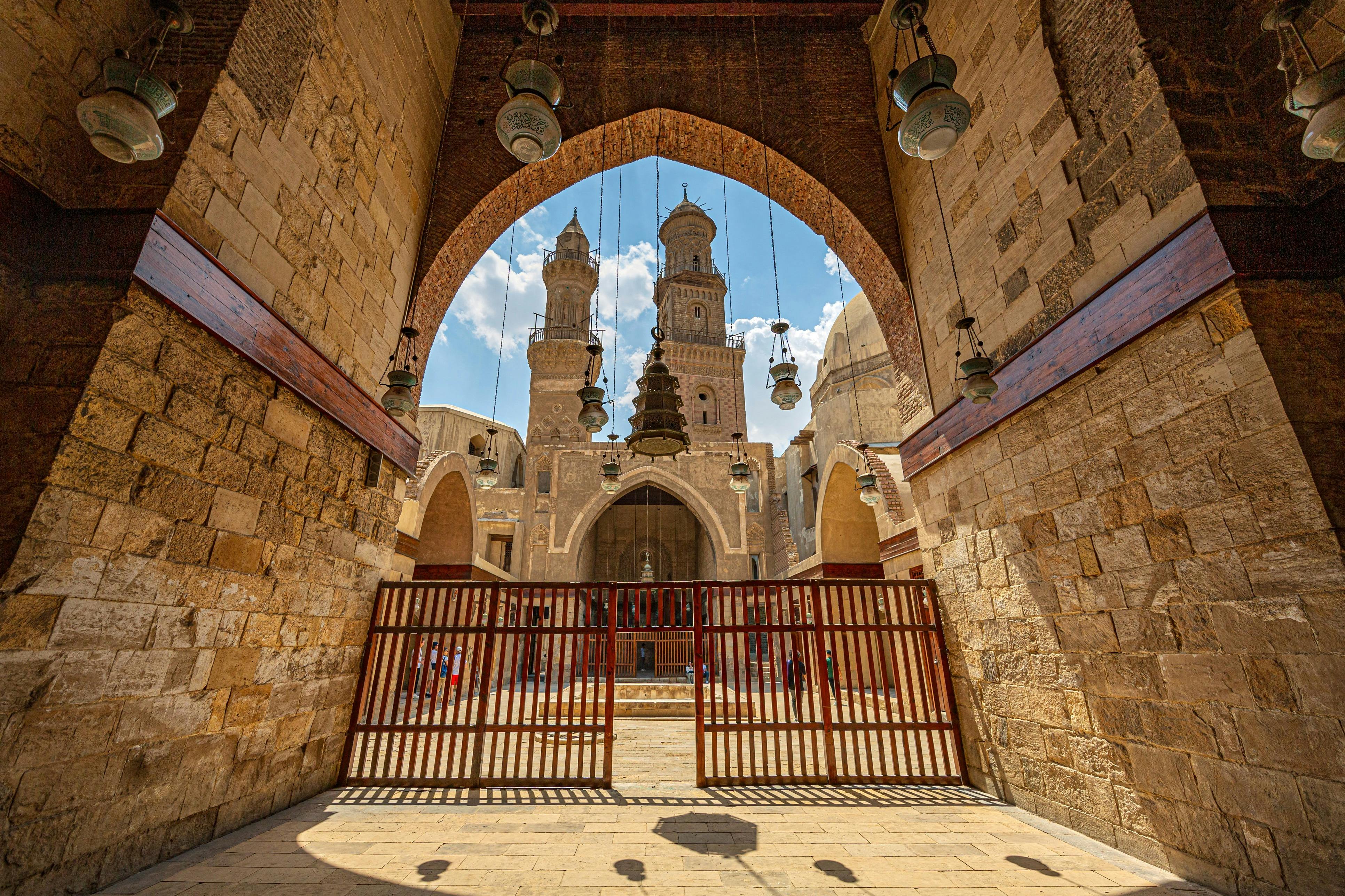 Вид на архитектурную арку, ведущую во внутренний двор с двумя высокими минаретами и подвесными фонарями.