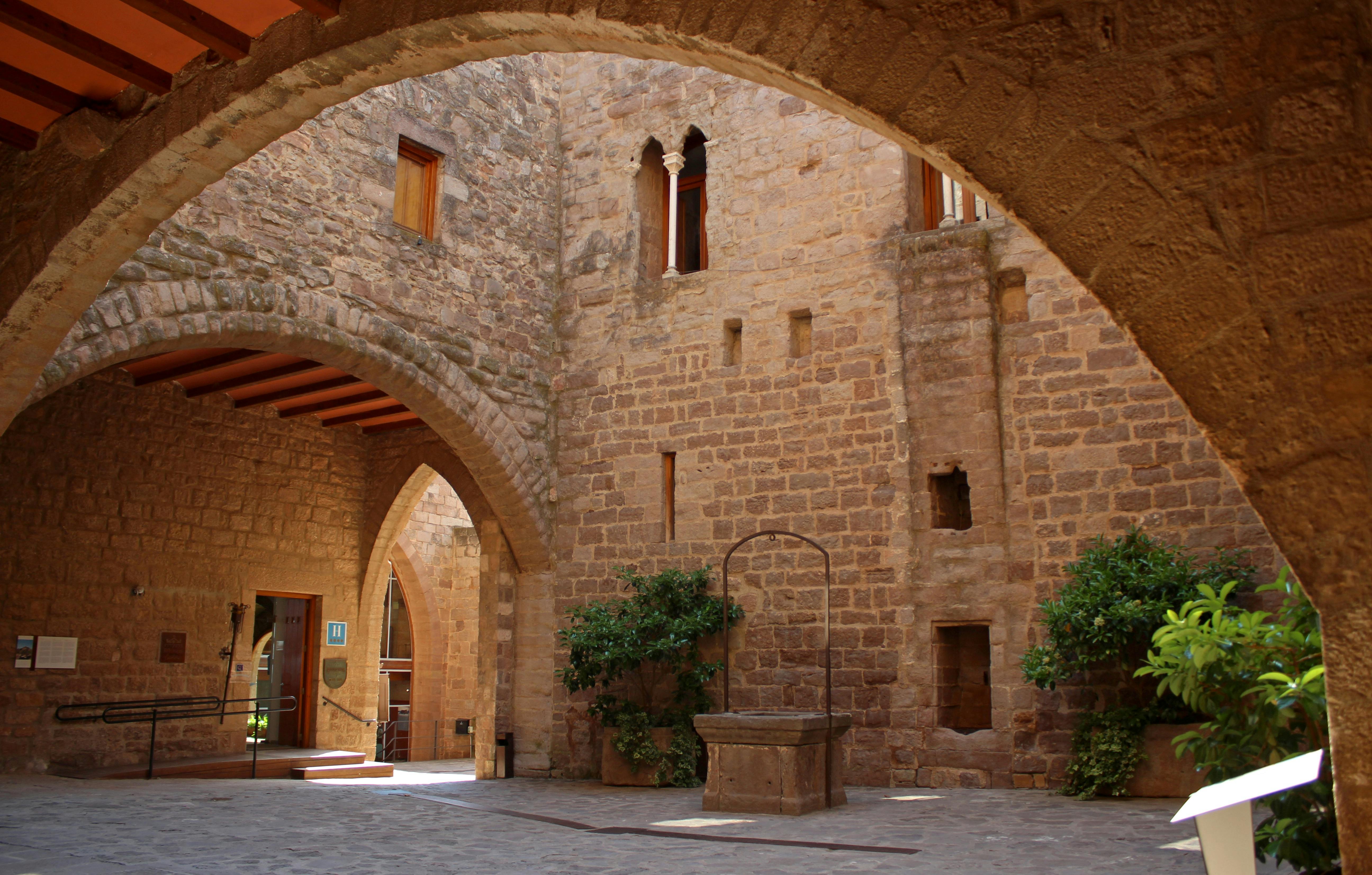 アーチ、井戸、緑のある石造りの中庭。 レンガの壁には小さな窓とアーチ型の開口部があります。