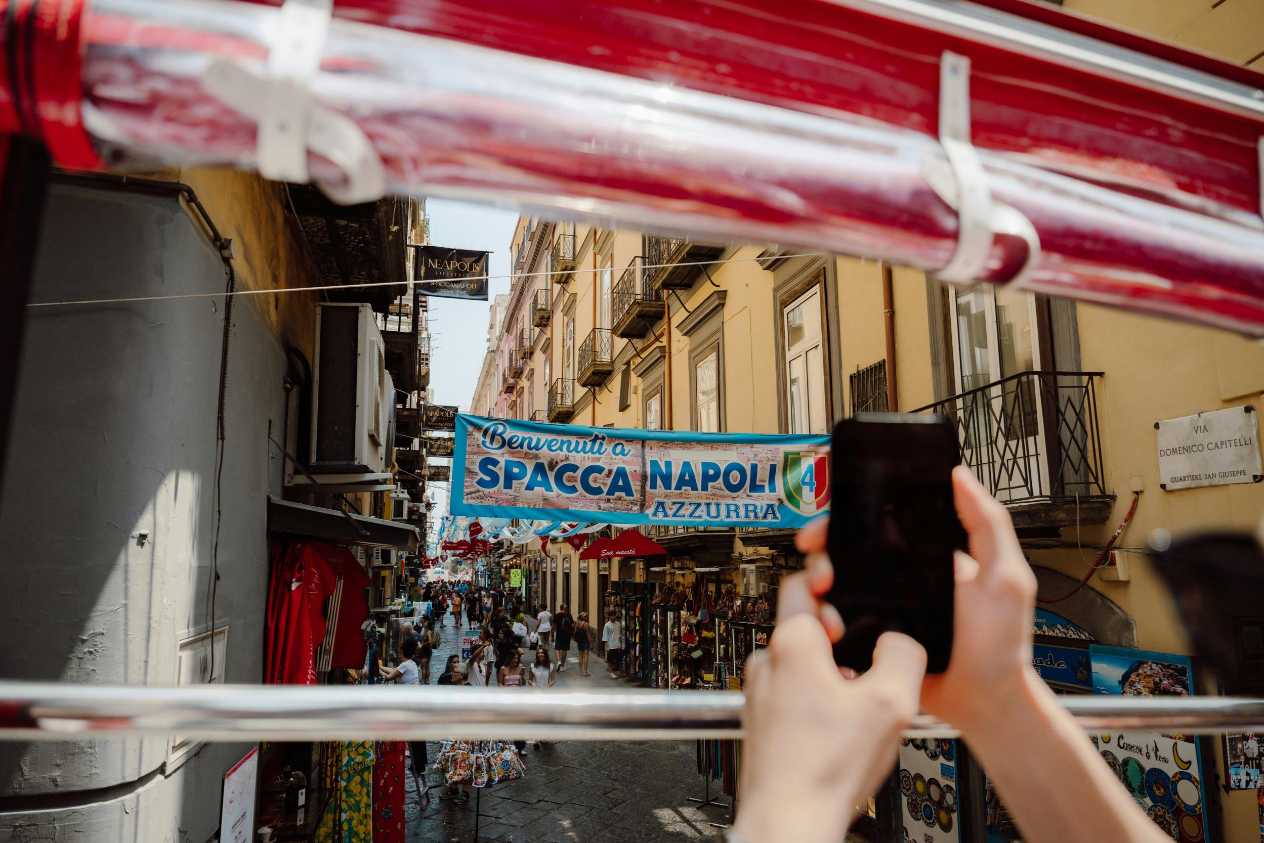 Una persona tiene in mano uno smartphone per scattare una foto di una strada affollata di Napoli, Italia, con uno striscione in alto che recita 
