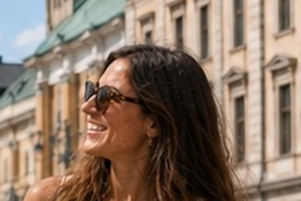 Three people smiling and talking in a sunny city square near a historic building with a clock tower.