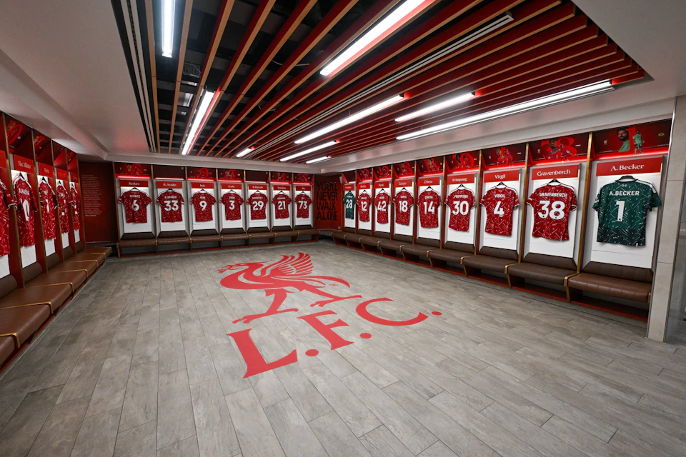 Locker room with red jerseys hung in individual spaces, a large LFC logo on the floor, and overhead lighting.