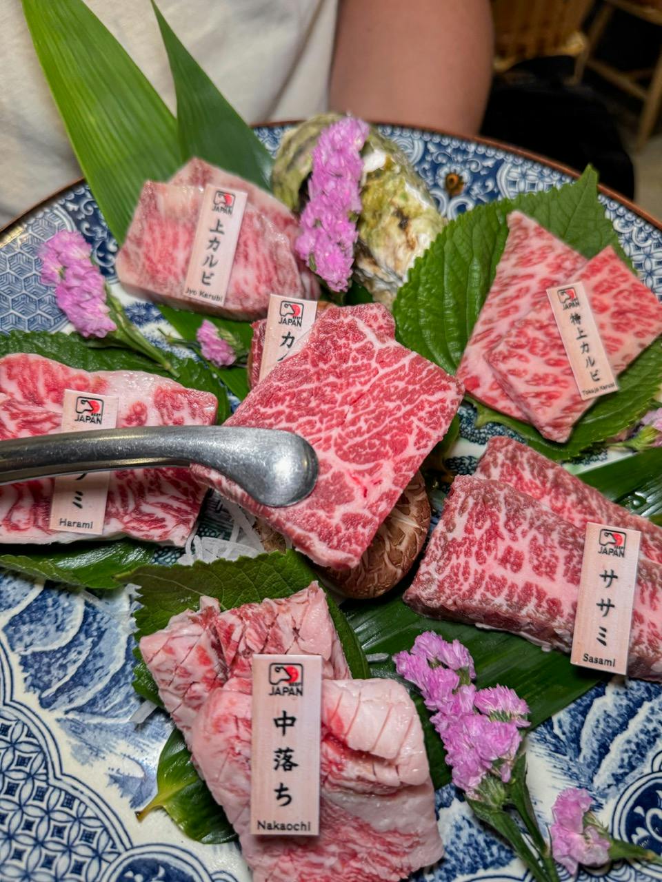 A plate of marbled raw beef cuts arranged on green leaves with decorative flowers and labels on a patterned dish.