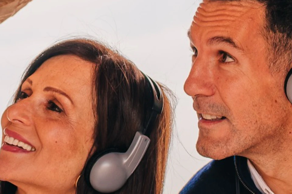 Two people wearing headsets and holding audio devices, exploring an architectural structure with curved designs.