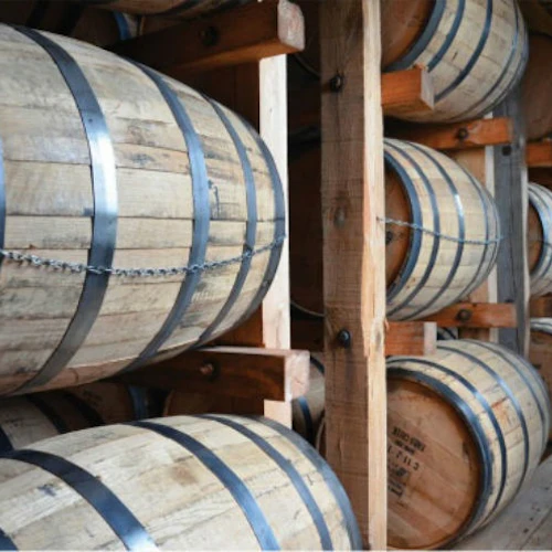 Wooden barrels stacked in rows on wooden racks inside a warehouse or storage area.