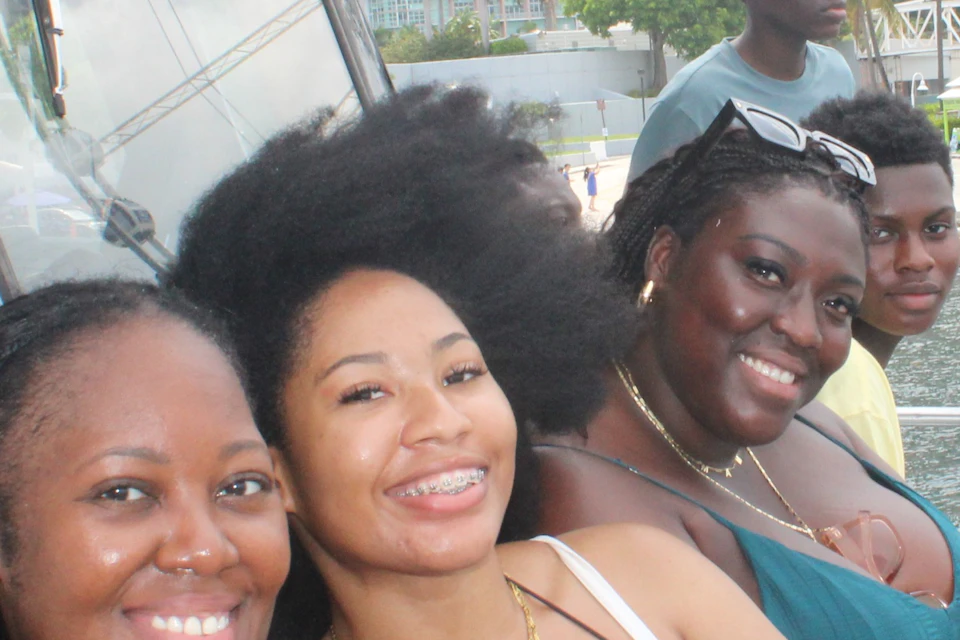 A group of people smiling on a boat with a city skyline and Ferris wheel in the background.