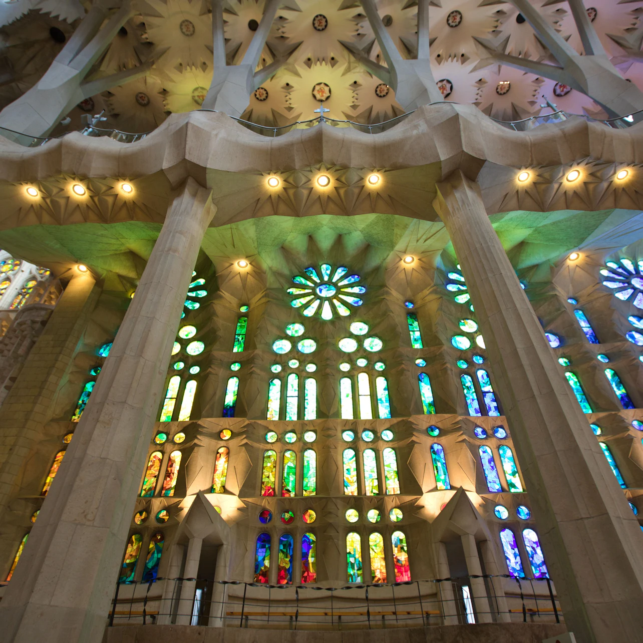 Interior view of a large cathedral with ornate stained glass windows and tall stone columns supporting a decorated ceiling.