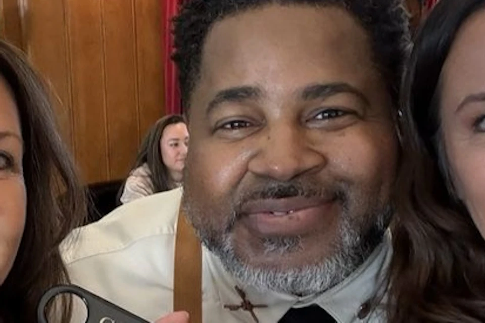Two women and a man smiling together indoors, holding Gold Bar Whiskey branded items.